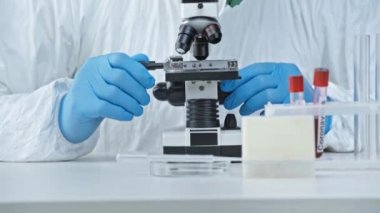 Tehlikeli madde giysisi içindeki bilim adamı test tüplerinin yakınında mikroskoptan bakıyor. 