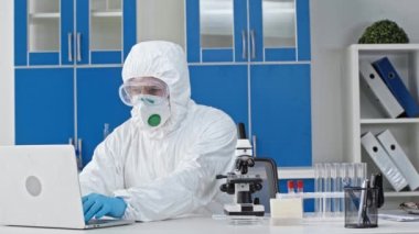 Erkek bilim adamı mikroskoptan bakıp laboratuvarda dizüstü bilgisayar kullanıyor.