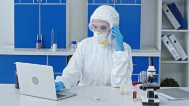 Laboratuvarda bilgisayarın yanında akıllı telefondan konuşan bilim adamı.