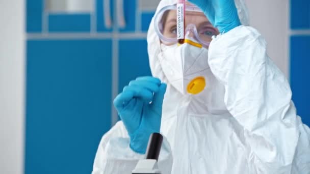 ハズマットスーツの科学者はコロナウイルスの文字でチューブを見て — ストック動画