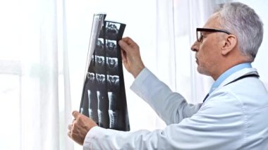 Beyaz önlüklü ve gözlüklü olgun bir doktor röntgene bakıyor.