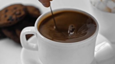 Ağır çekimde, beyaz bardakta koyu kahveyi karıştıran bir adam.