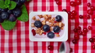 Yoğurdun yanında kaşık, granola ve cam içinde böğürtlen tutan bir adam.