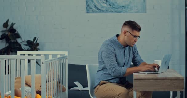 Отец Помощью Ноутбука Говорить Смартфоне Возле Детской Кроватки Младенцем — стоковое видео