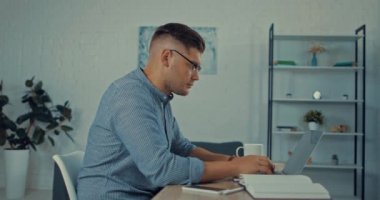 Laptop kullanan yakışıklı serbest çalışan, saate bakan ve akıllı telefonu alan.