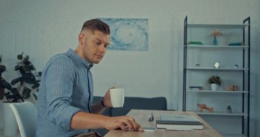 Yakışıklı serbest çalışan kahve içiyor, gözlük takıyor ve dizüstü bilgisayar kullanıyor. 