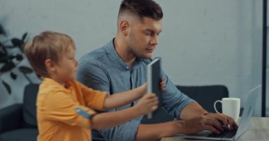 Şirin çocuk dizüstü bilgisayarı evde mutlu bir babanın yanına koyuyor.