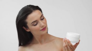 Elinde kozmetik kremi olan gülen çıplak bir kadın.
