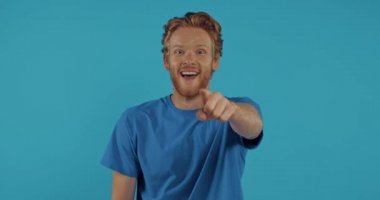 Adam parmağıyla işaret ediyor, baş parmağını kaldırıyor ve mavi üzerine gülüyor.