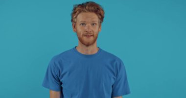 Kafası karışmış kızıl saçlı adam mavi renkte omuz silkiyor ve facepalm kullanıyor.