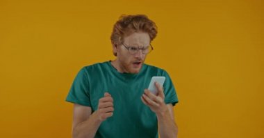 Gözlüklü kızgın kızıl saçlı adam sarı telefona izole edilmiş akıllı telefonu atıyor.