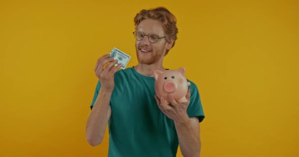 Feliz Ruiva Homem Colocando Dólar Porquinho Banco Isolado Amarelo — Vídeo de Stock