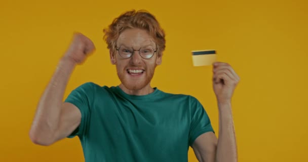 Счастливый Рыжий Человек Очках Держа Кредитную Карту Изолированы Желтый — стоковое видео