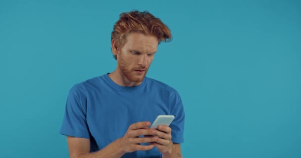 Triste Ruiva Homem Jogando Smartphone Isolado Azul — Vídeo de Stock