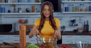 Kablosuz kulaklıklı mutlu kadın dans ediyor ve salata karıştırıyor.