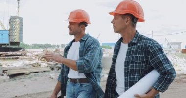 İnşaat alanında yürürken planlı konuşan sert şapkalı inşaatçılar.