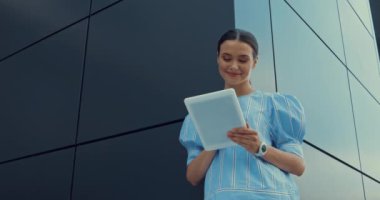 Binanın yanında dikilirken dijital tablet kullanan mutlu kadının düşük açılı görünümü