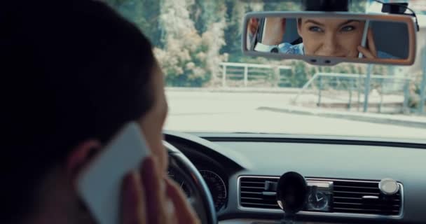 快乐的女人坐在车里 用智能手机说话 看着后视镜 — 图库视频影像