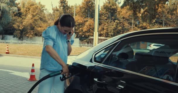 ガソリンスタンドで車を給油しながらスマホで話す幸せな女性ストック動画映像