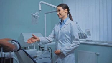 Klinikte hastayla el sıkışırken gülümseyen dişçi. 