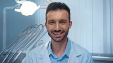 Gülümseyen dişçi klinikteki kameraya jest yapıyor. 