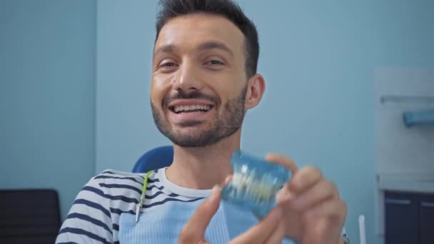 Sonriente Hombre Mostrando Como Mientras Sostiene Los Dientes Modelo Clínica — Vídeo de stock