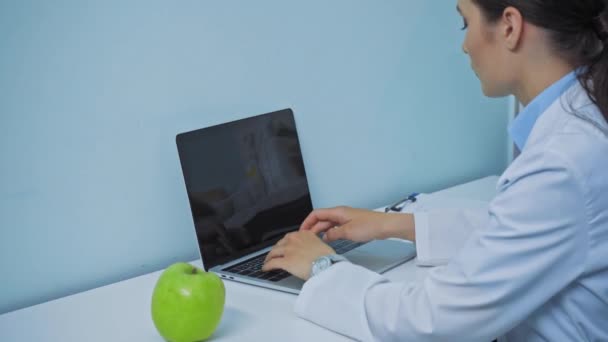 牙科医生在靠近苹果和剪贴板的地方使用笔记本电脑 — 图库视频影像