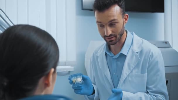 歯科の患者に歯モデルを示すラテックス手袋の歯科医 — ストック動画