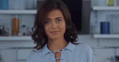 Esmer kadın mutfakta kameraya bakıyor. 