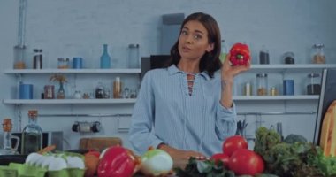 Kadın kameraya konuşuyor ve mutfak masasında ham malzemeler gösteriyor. 