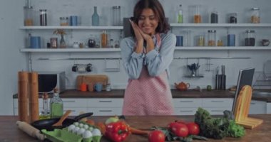 Mutfak masasında çiğ sebzelerin yanında duran kadın. 