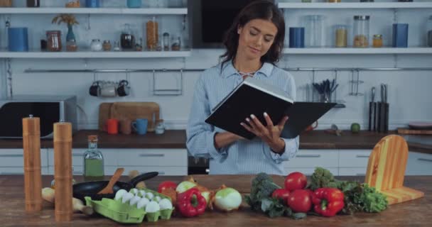 在厨房桌上新鲜蔬菜旁边看书的女人 — 图库视频影像
