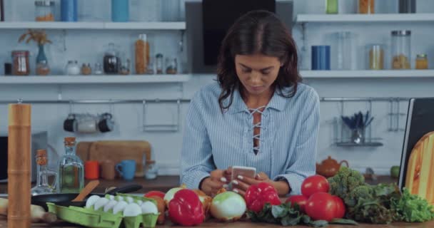 厨房里新鲜蔬菜旁边用智能手机的年轻女人 — 图库视频影像