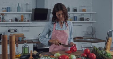 Genç bir kadın mutfakta salata için kırmızı biber kesip yiyor. 