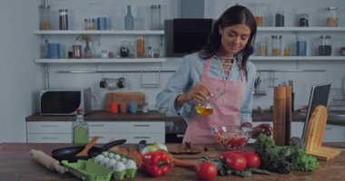 Sebzelerin yanında taze salataya yağ ve mutfak masasında yumurta ekleyen bir kadın. 