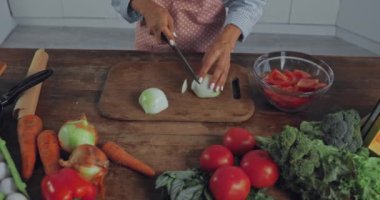 Mutfakta olgunlaşmış sebzelerin yanında soğan doğrayan kadın görüntüsü. 