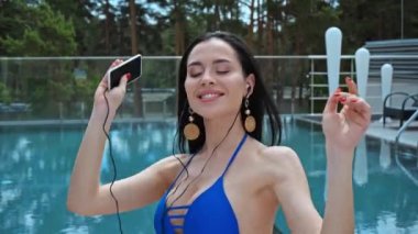 Kulaklıklı, müzik dinleyen ve havuz başında akıllı telefon tutan memnun bir kadın.