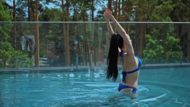 水着姿のセクシーな女性がプールの青い水の中を歩くストック動画映像