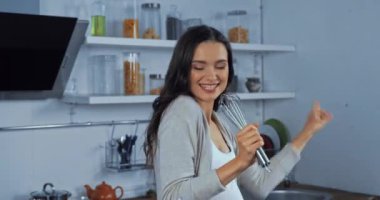 Hamile kadın mutfakta çırpıcı çırpıcısıyla şarkı söyleyip dans ediyor. 