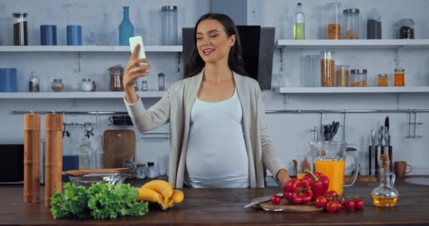 在厨房靠近蔬菜的地方拿智能手机自拍的孕妇 — 图库视频影像