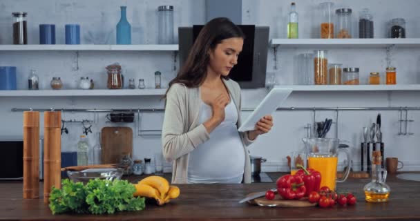 在厨房桌上新鲜蔬菜旁边使用数码平板电脑的孕妇 — 图库视频影像