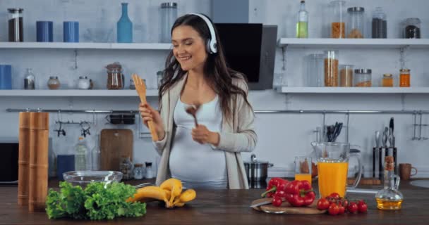 在厨房里 戴着耳机的孕妇在蔬菜旁跳舞唱歌 — 图库视频影像