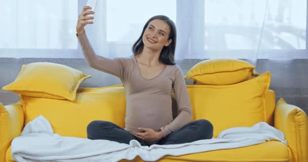 妊娠中の女性取ります自己撮影とともにスマートフォンでリビングルーム — ストック動画