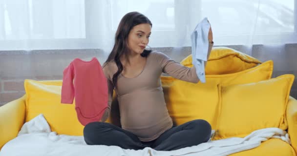 妊娠中の女性保持ベビー服オンソファ — ストック動画