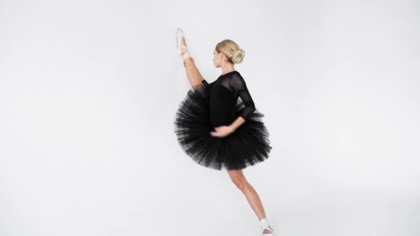 年轻的芭蕾舞演员 身穿黑色燕尾服 在白色背景下靠墙伸展腿 — 图库视频影像