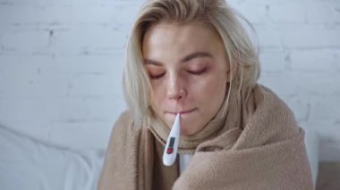 Hasta kadın ısıyı dijital termometreyle ölçmek için battaniyeye sarılmış. 