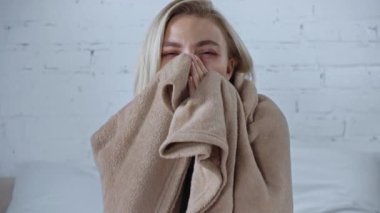 Genç hasta kadın battaniyeye sarılıp evde öksürüyor.