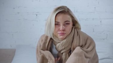 Hasta sarışın kadın evinde yumuşak battaniyeye sarılıyor.