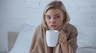 Elinde çay fincanı ve uzaktan kumandayla hasta genç bir kadın. 