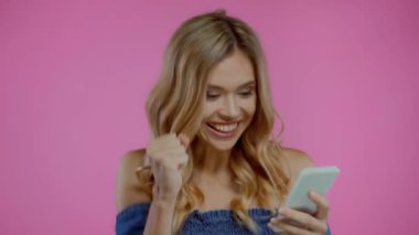 Heyecanlı sarışın kadın evet derken mor renkte izole akıllı telefon kullanıyor.